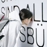 A woman is looking through little wholes in a textwall, which says: All citizens are equal before the law.